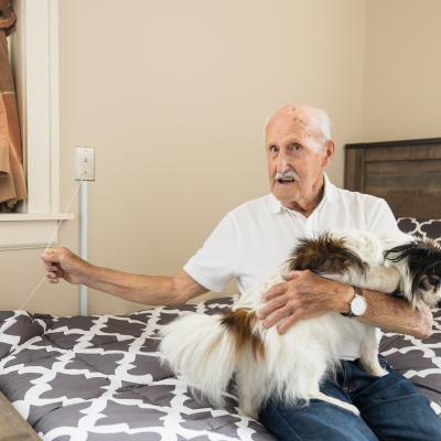 Champlain Valley Senior Community resident holding his dog while sitting on bed.