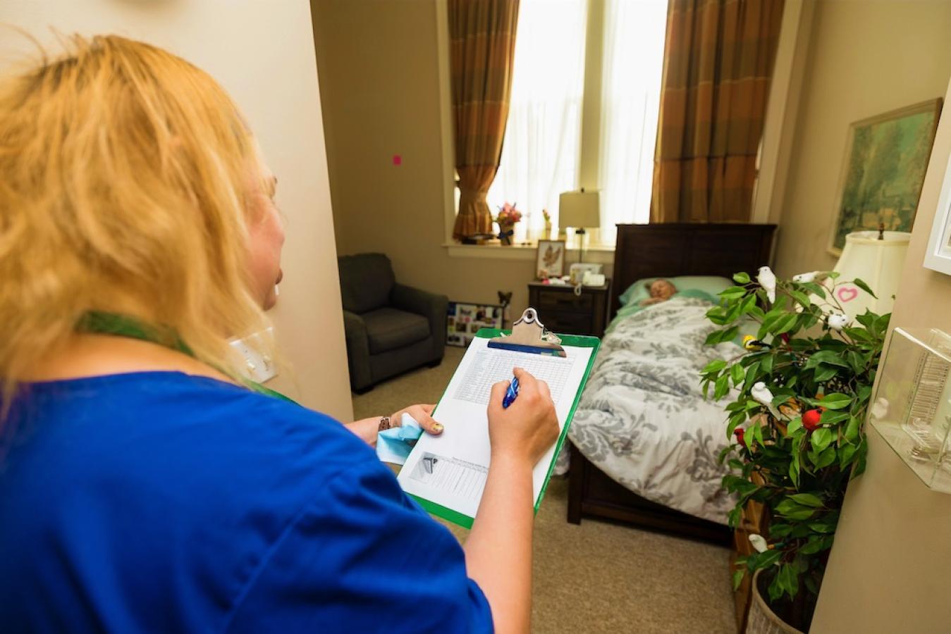 A nurse checking in on a resident in their bed.