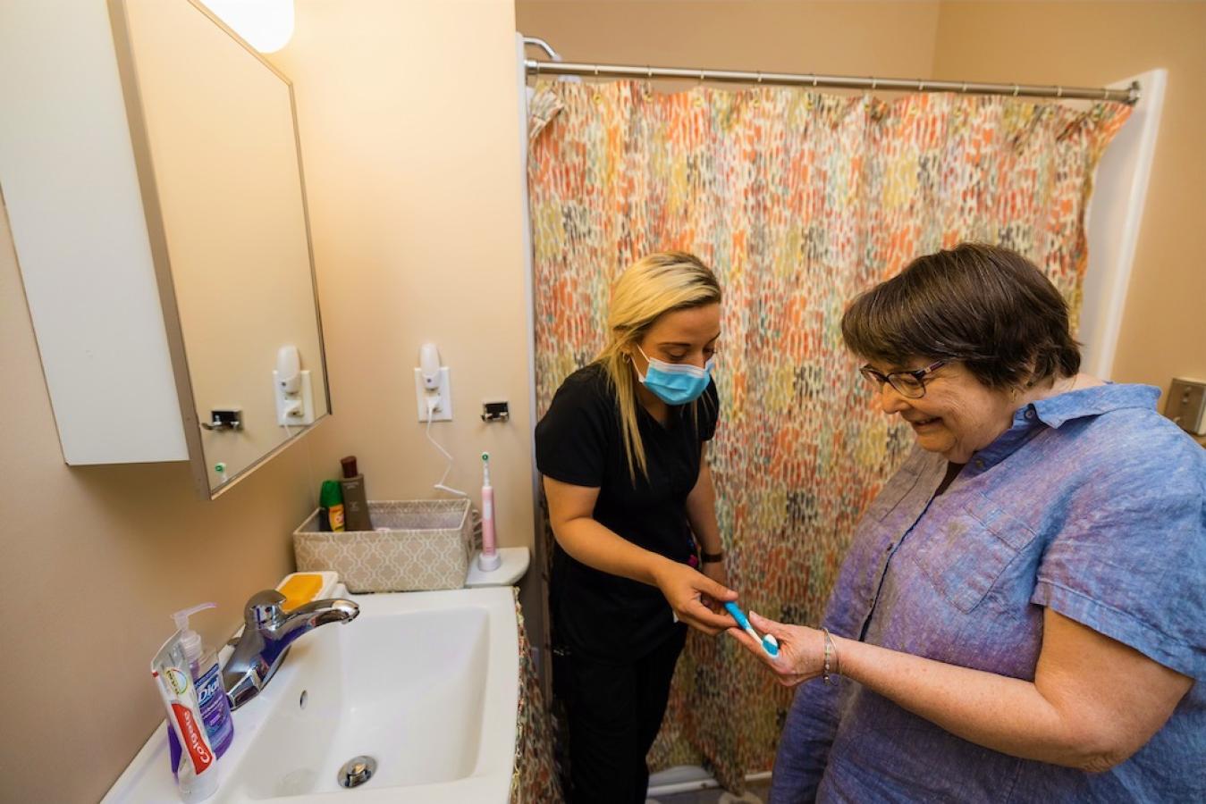 A nurse helping a resident get toothpaste in their bathroom.