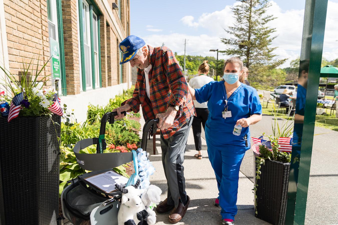 A resident using a walker being helped into the facility by a resident nurse.