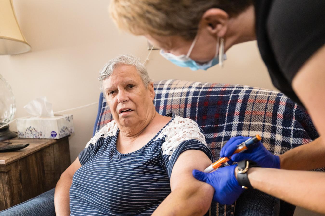 A nurse administering medication for a patient that is sitting down.