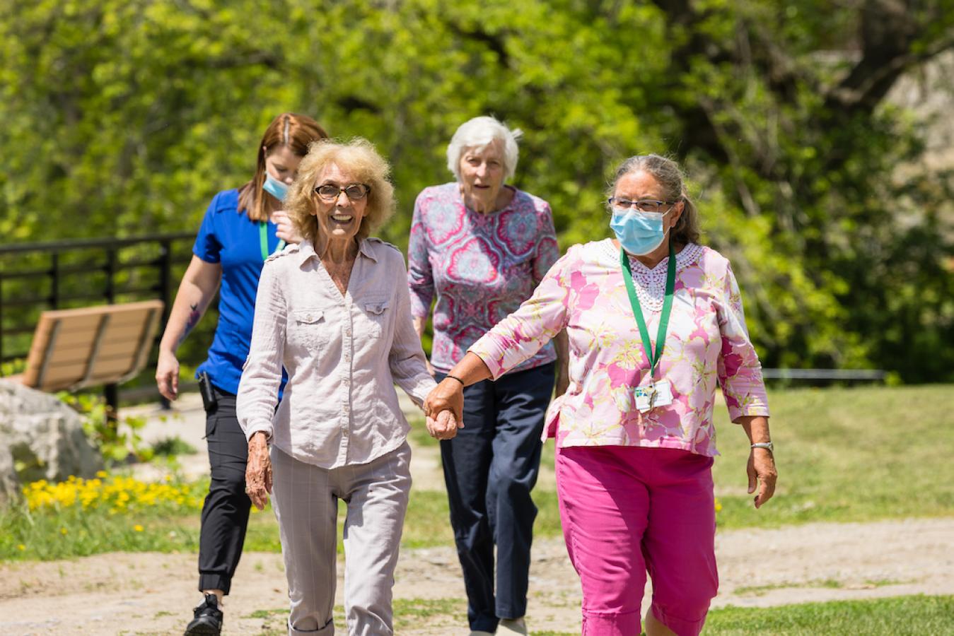 Nurses and residents outside on a walk, there is a park bench behind the on a riverside.