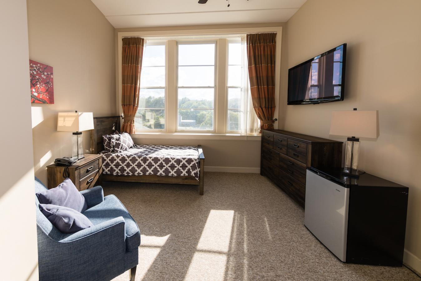 An example of a resident room, with a bed, side chair, tv, and dresser.