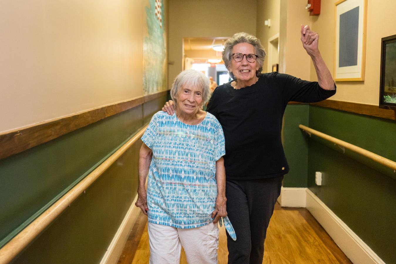 Two residents walking in a hallway, one has an armed raised. Both are smiling.