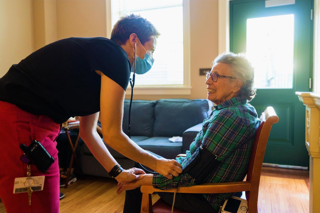 Nurse providing care to resident seated in chair. 