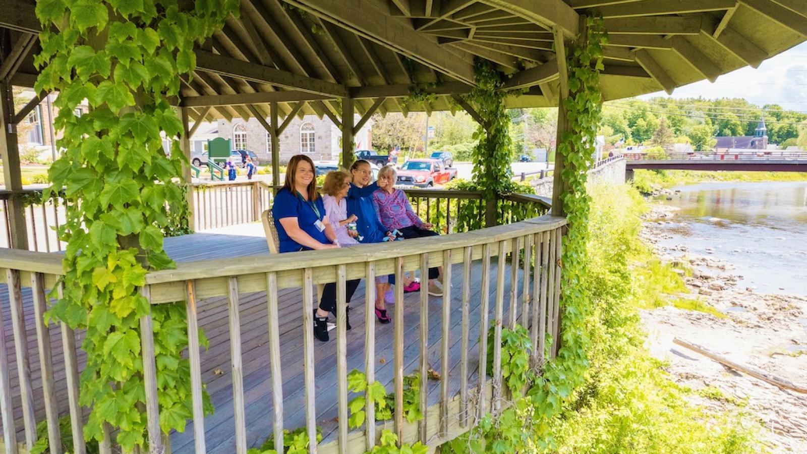 Two residents with two nurses, outside under a gazebo looking at the river.
