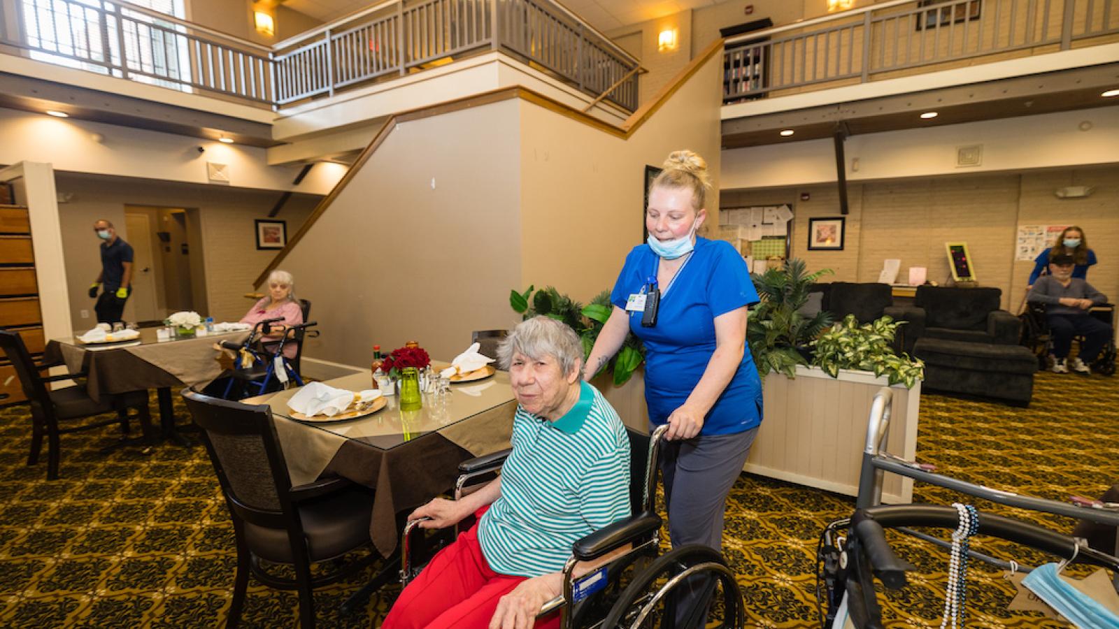 A nurse helping a resident in a wheelchair, enter the cafeteria.