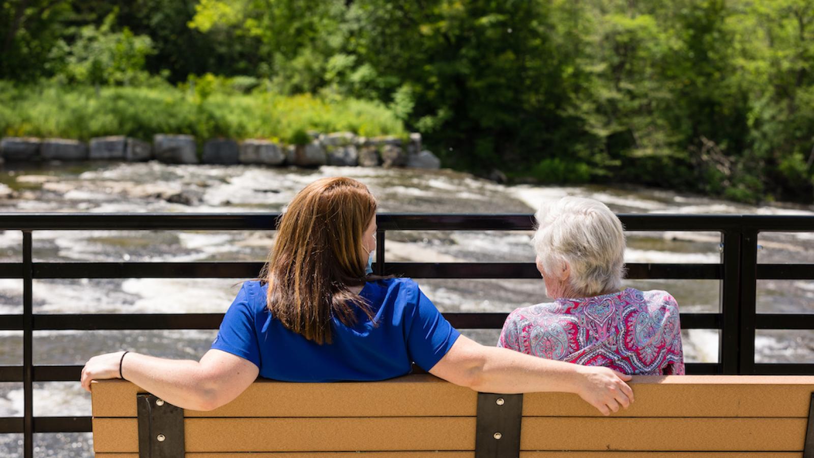 A resident and nurse sitting outside on a park bench.