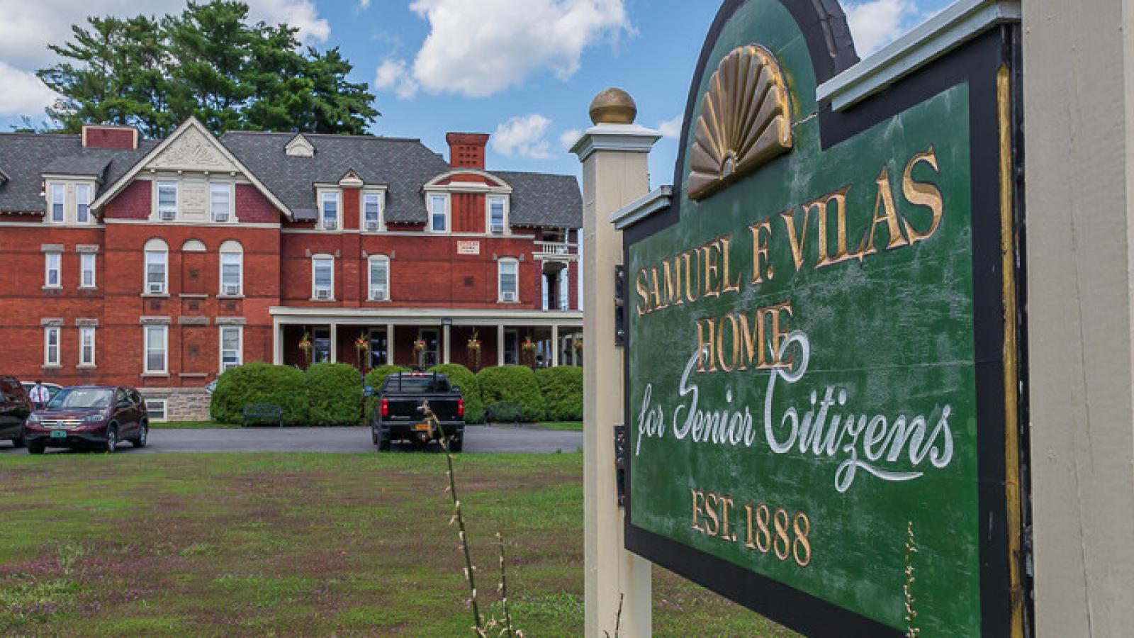 Vilas home sign with the historic red brick Vilas Home in the distance