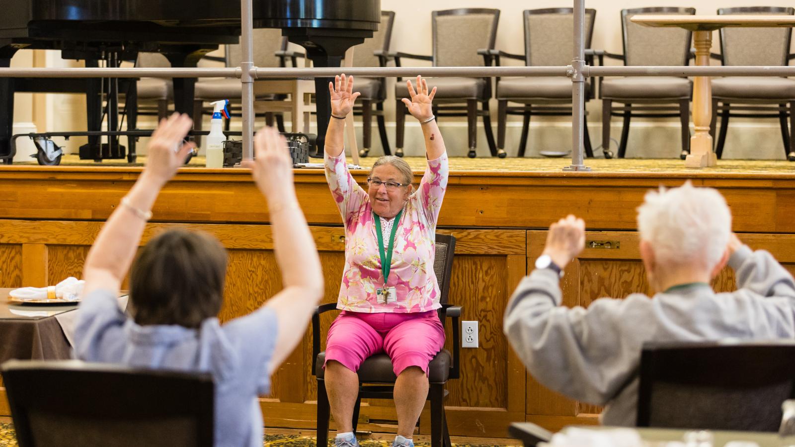 Seated woman leading group exercise class for seniors. 