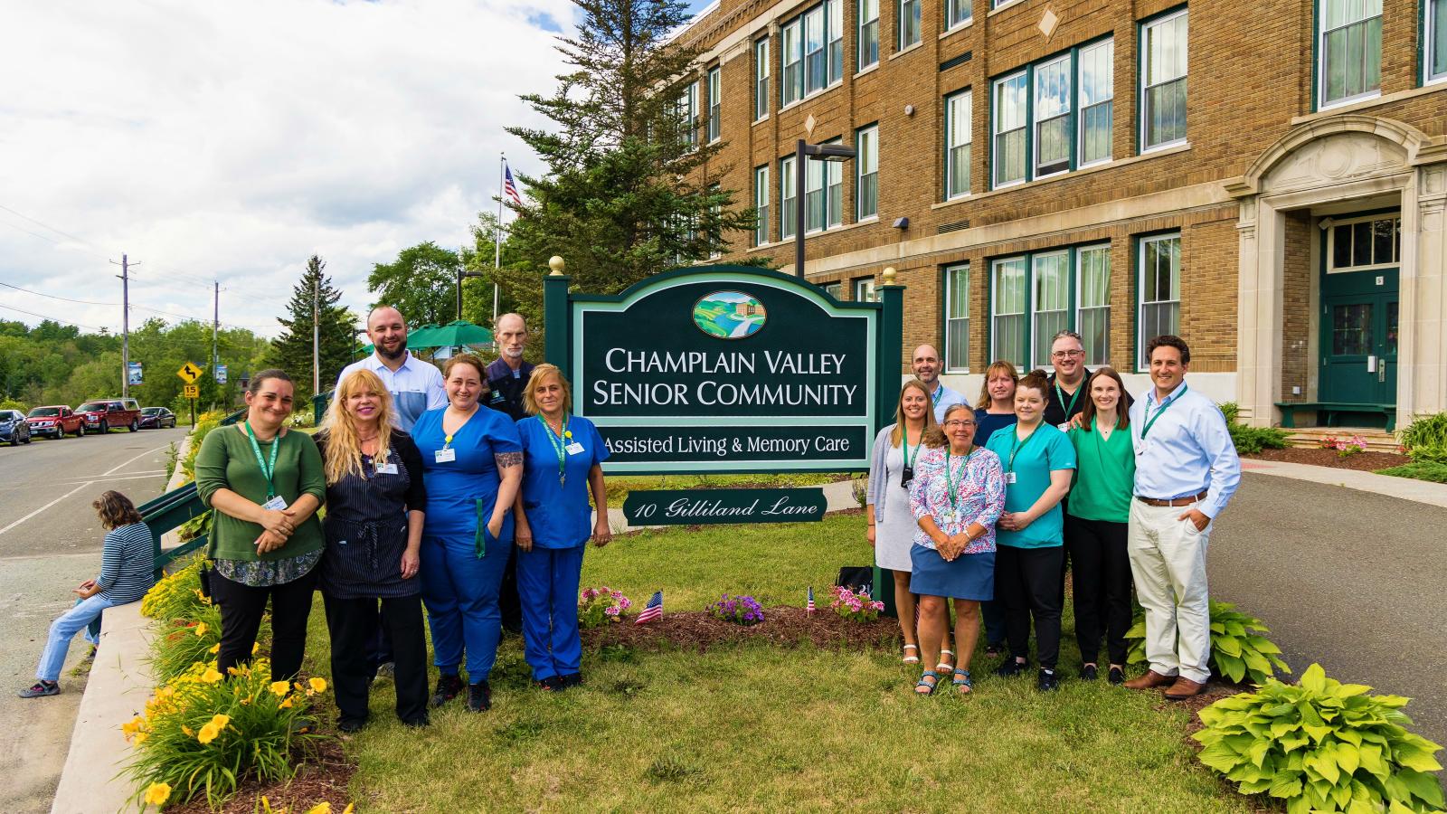 Senior living care team standing next to Champlain Valley Senior Community sign.