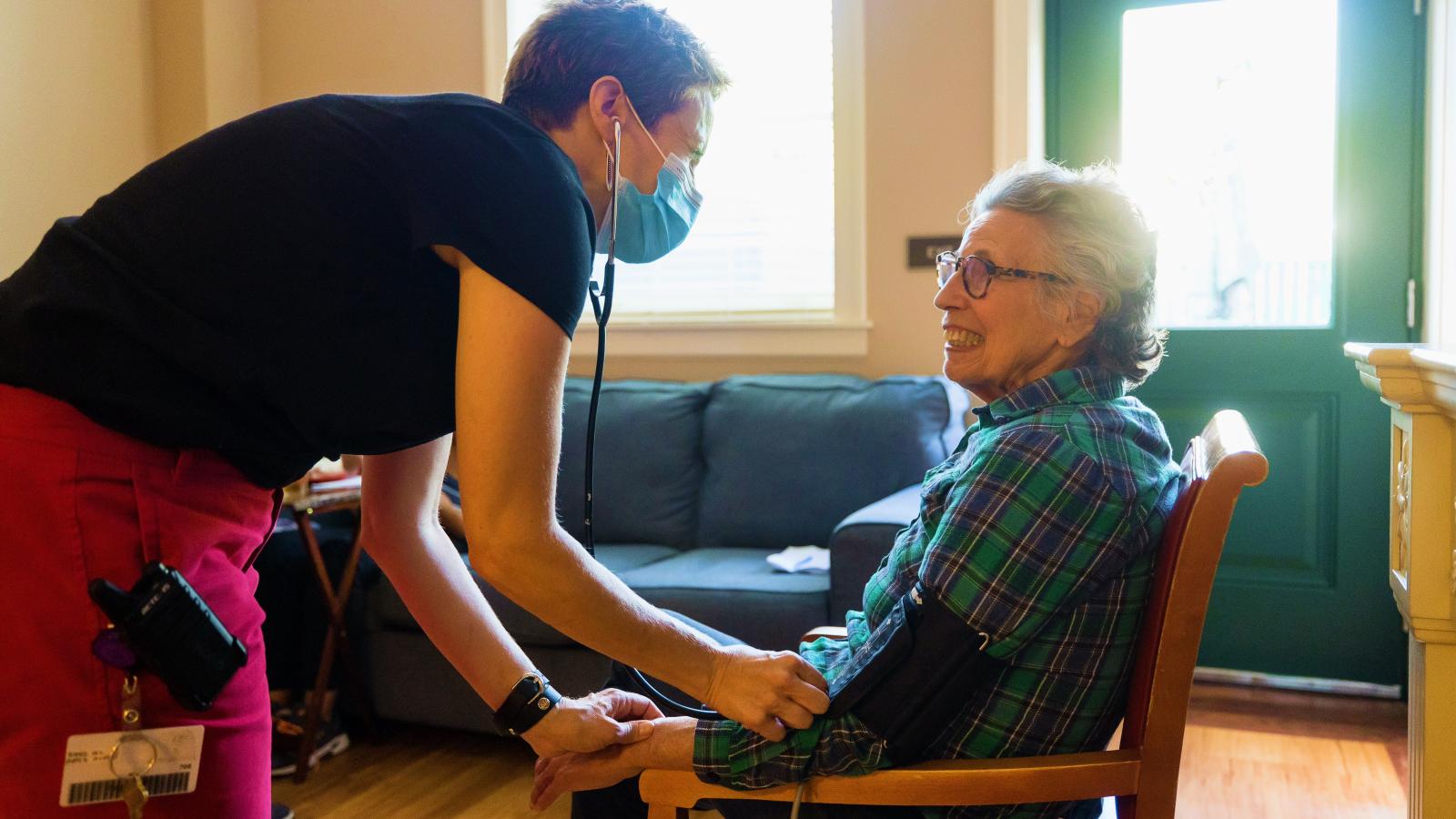 Staff checking blood pressure of female resident sitting in a chair.