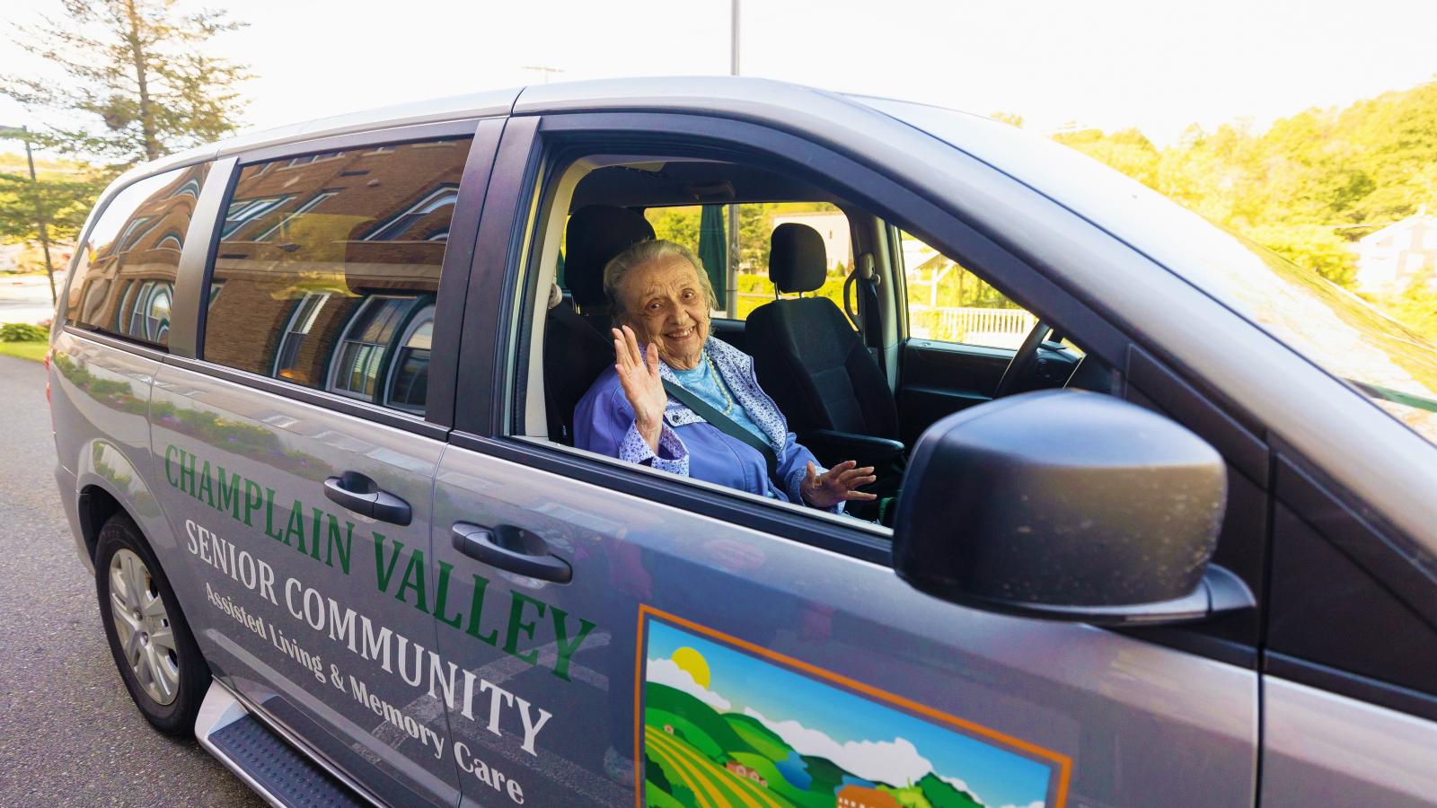 Happy senior waving from the transportation van for Champlain Valley Senior Community