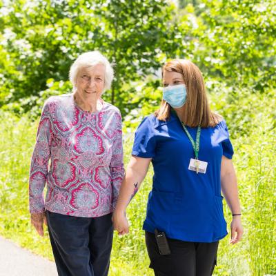 A resident walking with a nurse holding hands, outside.