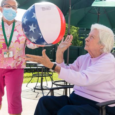 A resident and nurse throwing an American flag beach ball outside.