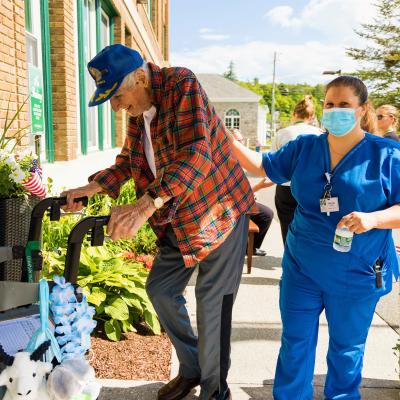 Male resident with walker followed by nurse walking into building.