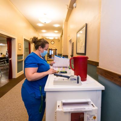Nurse standing in a hallway in front of a cart, reviewing a binder of documentation.