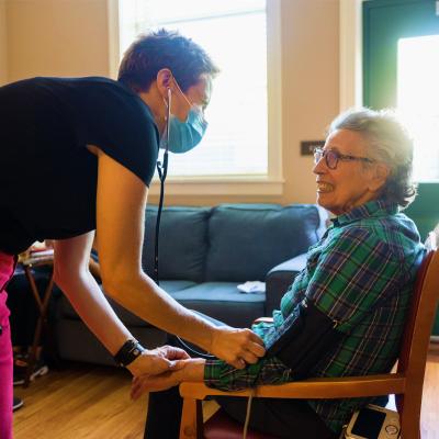 Nurse taking blood pressure of female resident seated in chair