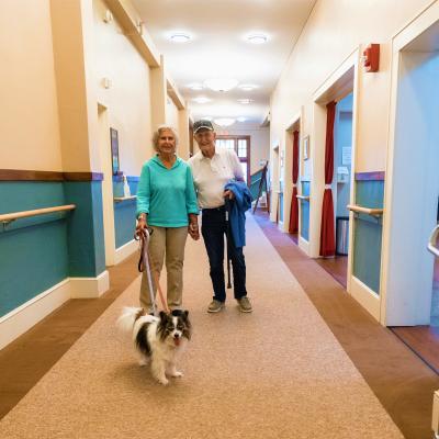 Man and woman walking dog in the hallway of our assisted living facility. 