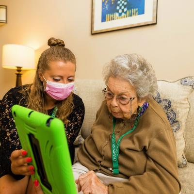 Staff member holding a lime green iPad for a senior female resident.