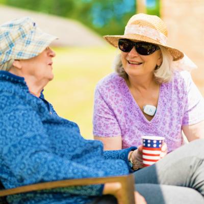 Woman in hat visiting with a senior resident while sitting outside. 