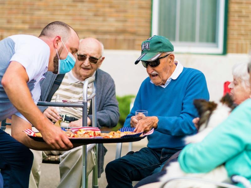 Three residents being delivered small snacks while sitting at an outdoor gathering at our facility.