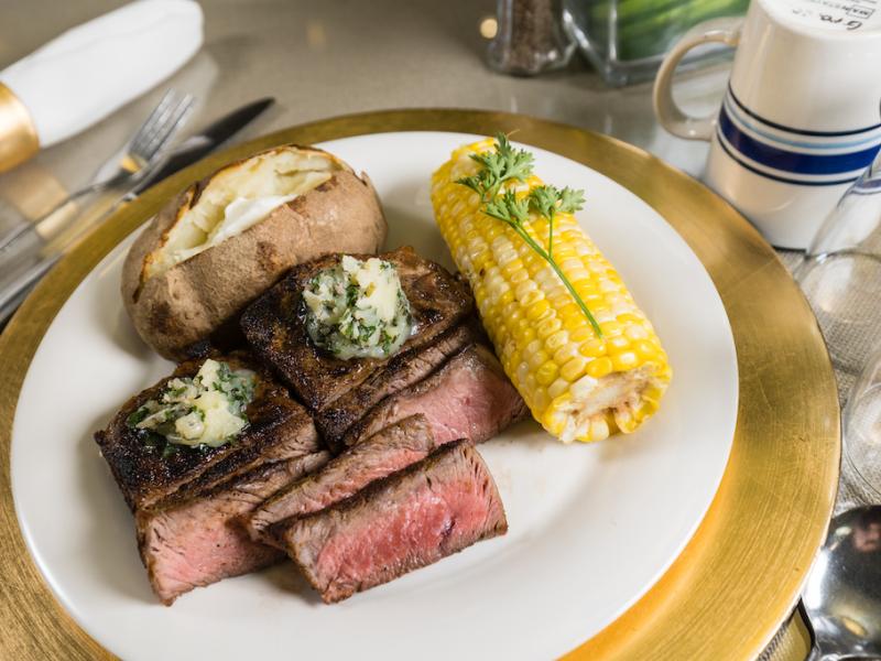 A steak and corn dinner, on a white and gold dinner plate.