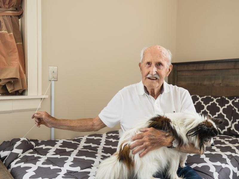 A resident and his dog seated on a bed. 