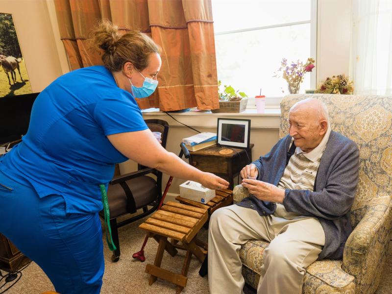 Nursing staff caring for male resident seated in chair. 